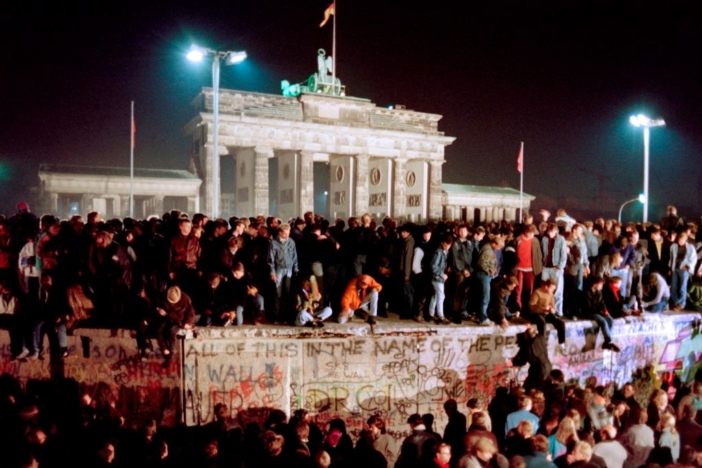 A large crowd of people celebrates atop the Berlin Wall near the Brandenburg Gate, marking the historic fall of the Berlin Wall in November 1989