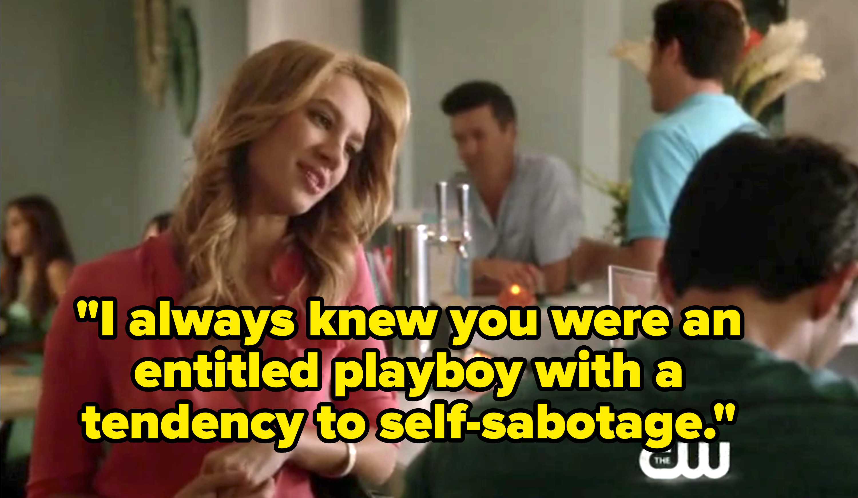 A woman sits at a bar talking to a man with his back to the camera in a scene from a CW TV show. People are in the background