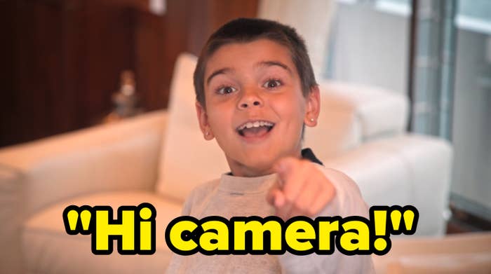 Child smiling and pointing towards the camera inside a living room with white furniture