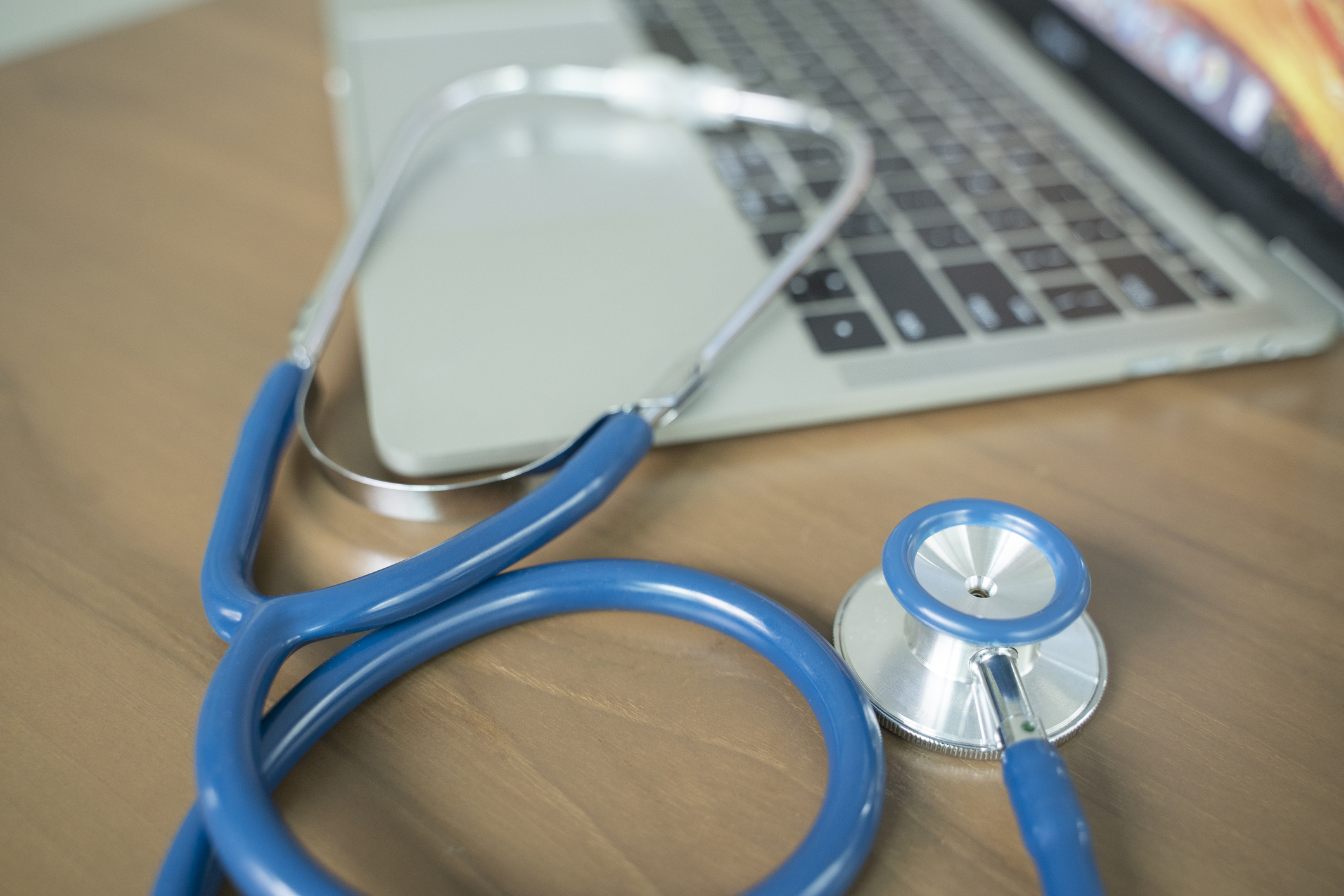 A stethoscope lies on a wooden desk next to an open laptop
