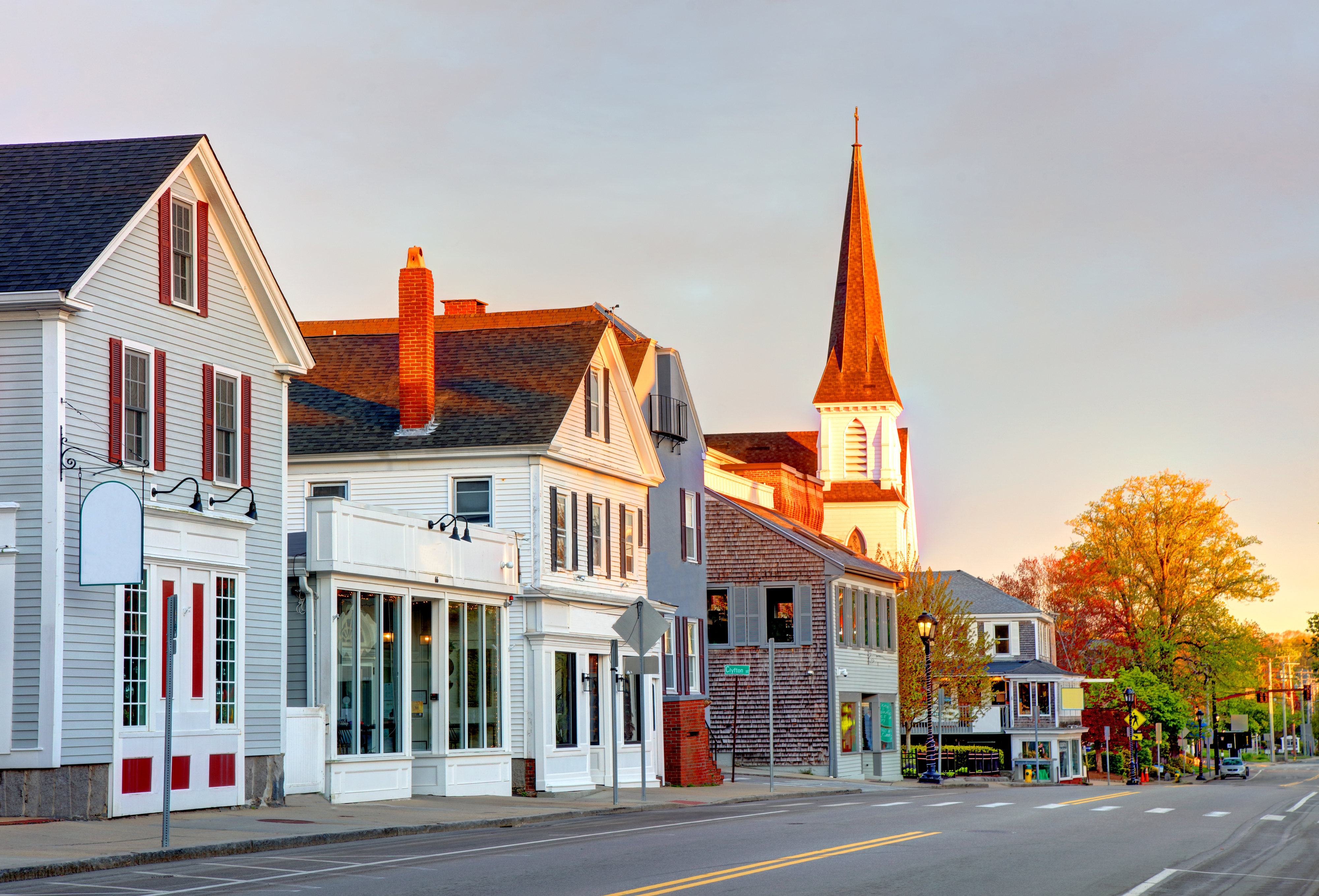 A quaint small-town street with various shops and a tall church steeple basking in early morning light