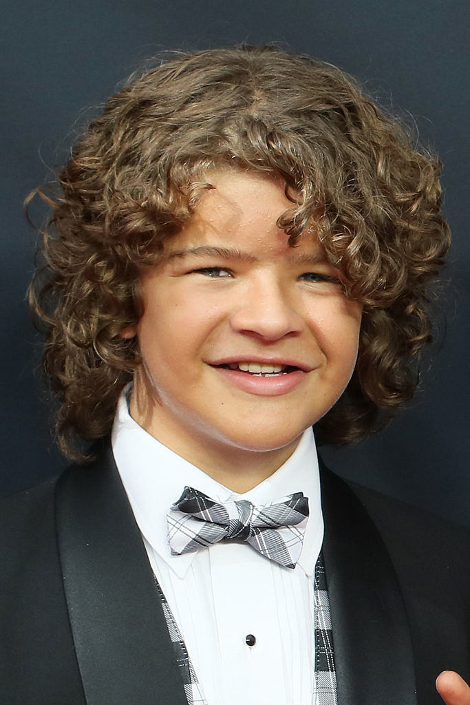 Gaten Matarazzo at a formal event in a black tuxedo with a plaid bow tie, smiling at the camera