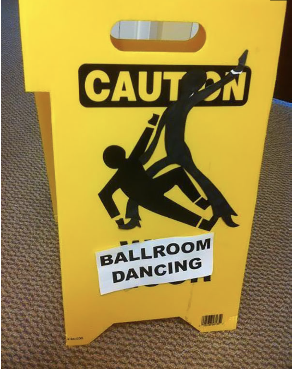 A yellow caution sign displays a humorous graphic of two figures dancing with the text "BALLROOM DANCING" on top of the original warning
