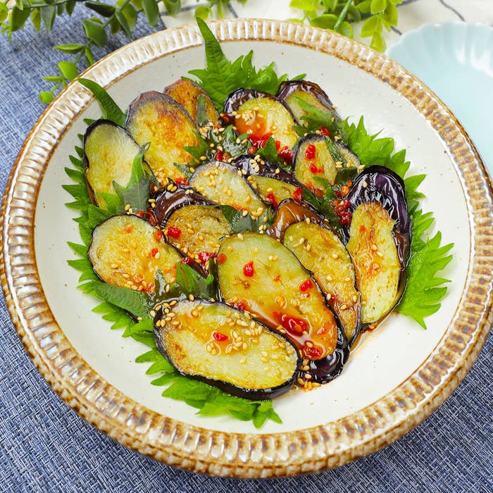 皿に盛られたナス、ゴマと赤唐辛子がトッピングされている。デザイン性のあるプレートに盛り付けられている。