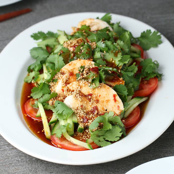 皿に盛られた鶏肉、トマト、きゅうり、香菜がたっぷりのアジア風サラダ。ゴマがかかっている。