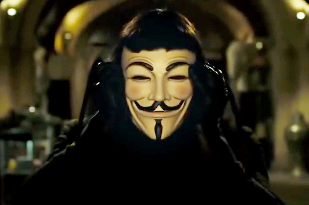 Person wearing Guy Fawkes mask, reminiscent of the movie "V for Vendetta", adjusting the mask with both hands in a dimly lit room