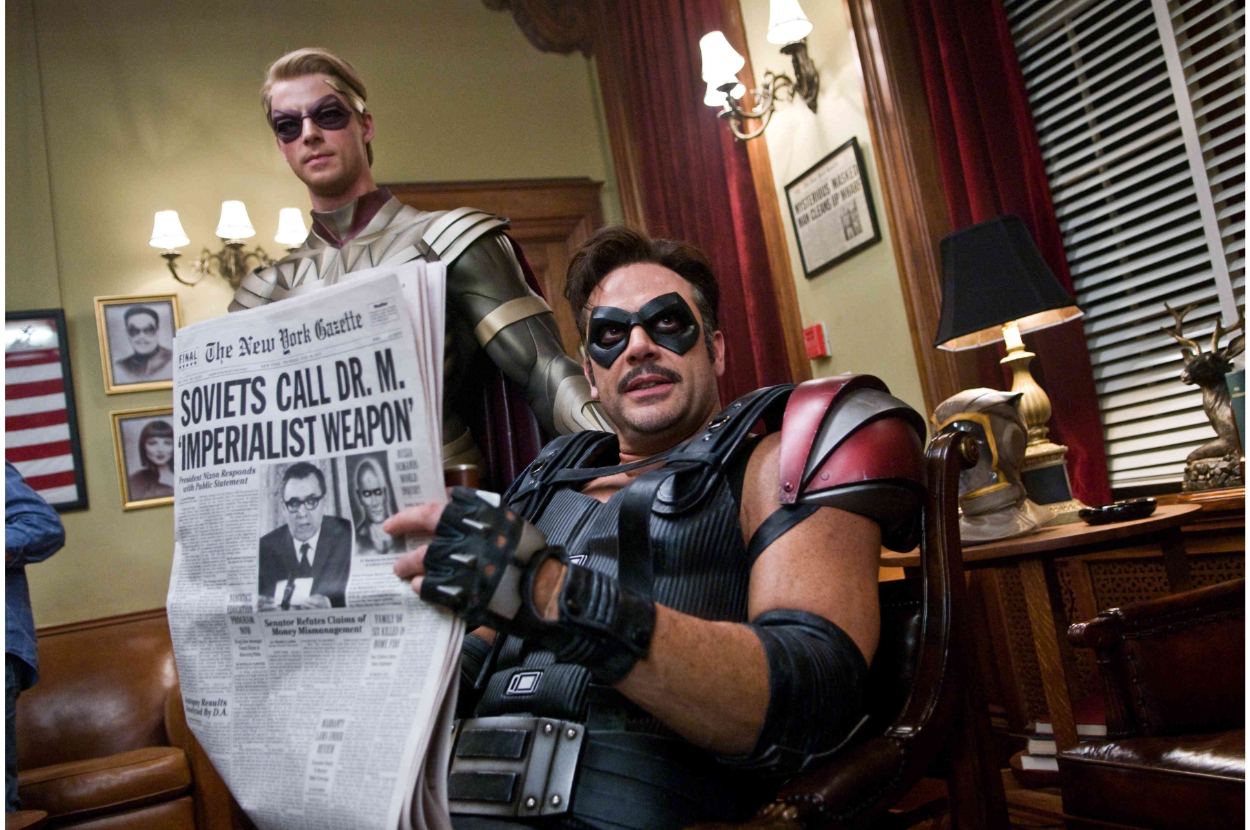 Two people in superhero costumes, one holding a newspaper with the headline "Soviets Call Dr. M. ‘Imperialist Weapon’.”