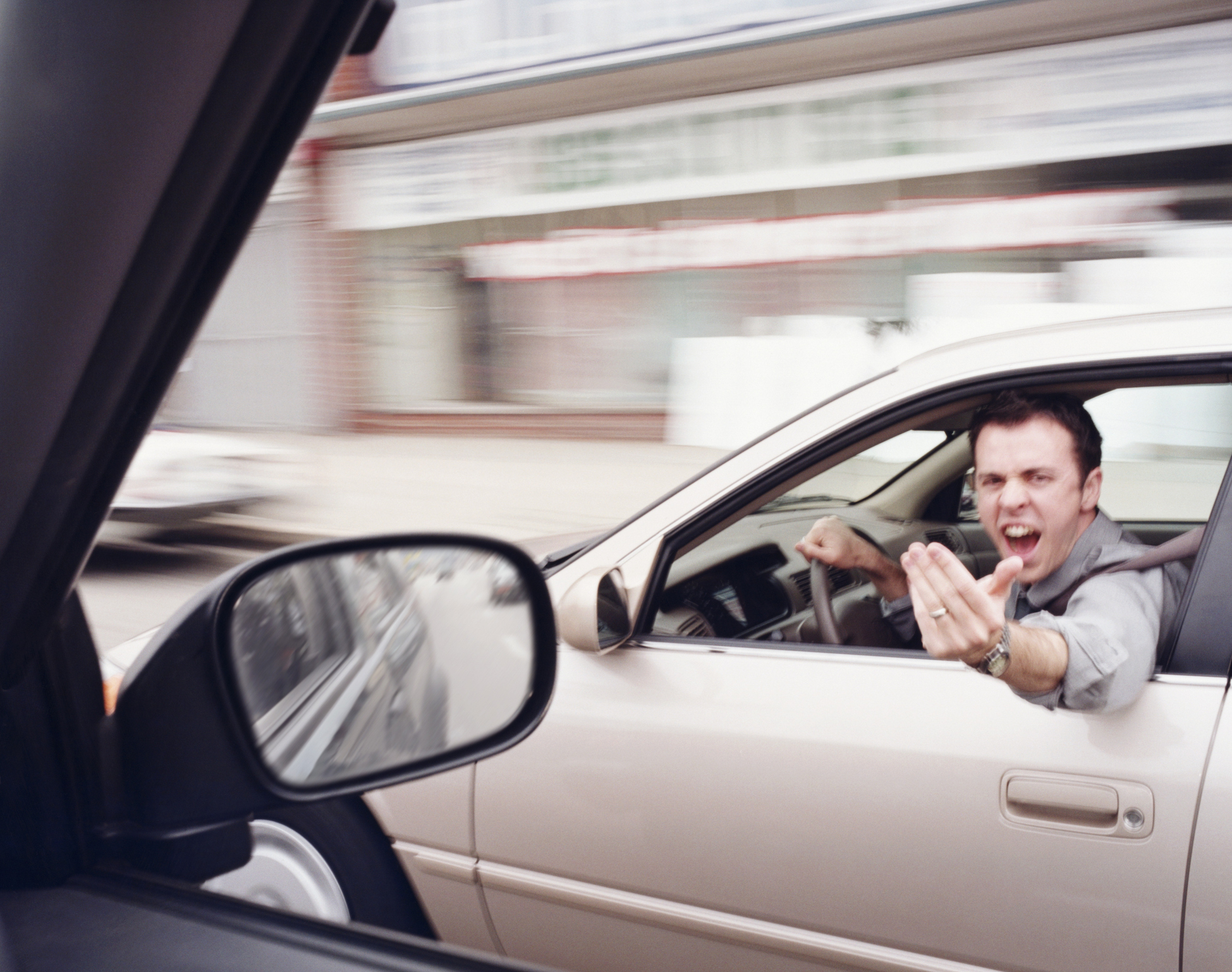 A man in a car angrily gestures at another driver through his window