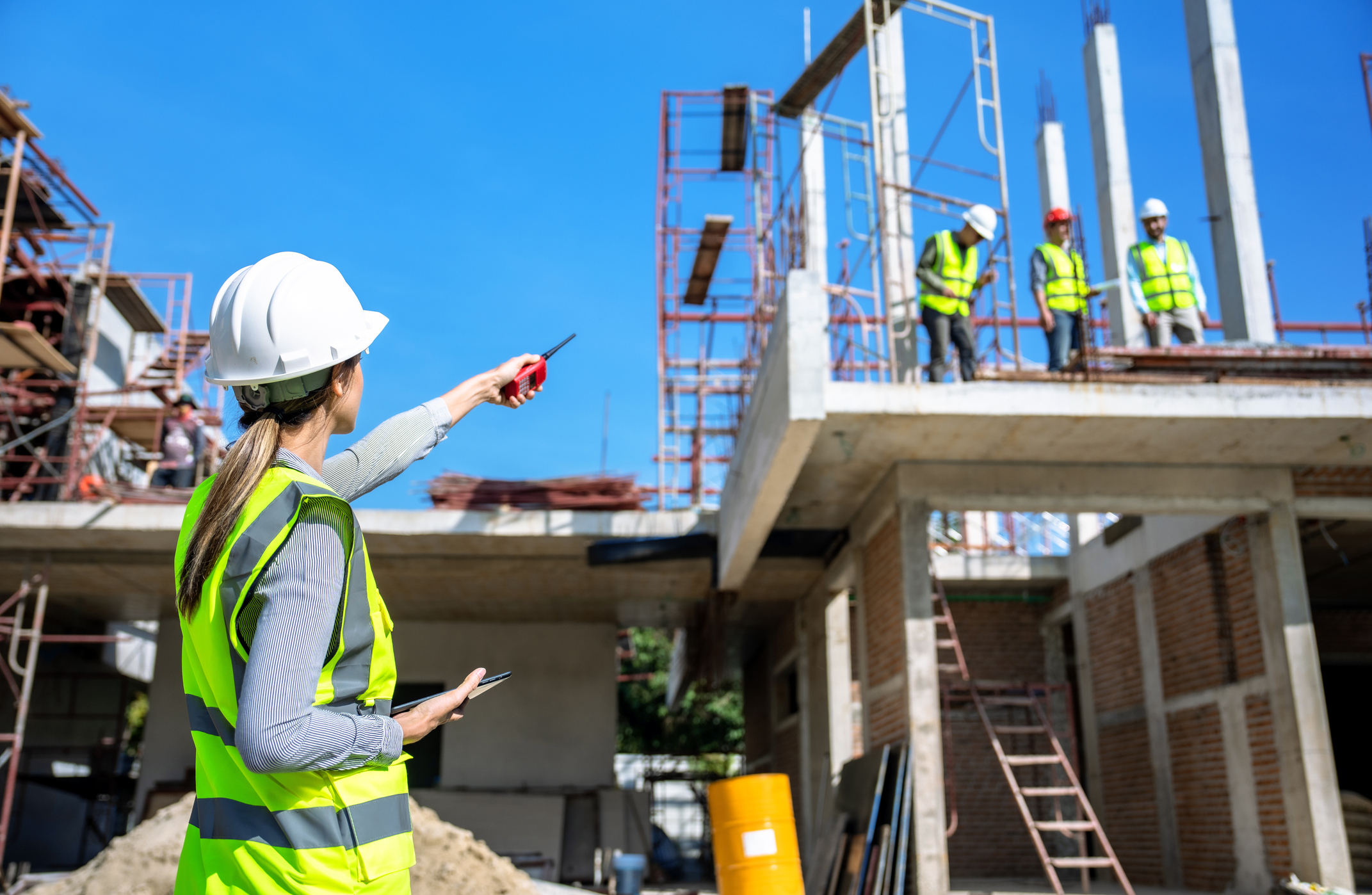 Construction workers on-site, one person in a hard hat and reflective vest directing others standing on an unfinished building structure