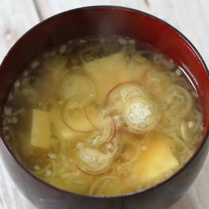 赤い器に入ったみそ汁、豆腐とみょうがの具が見える。