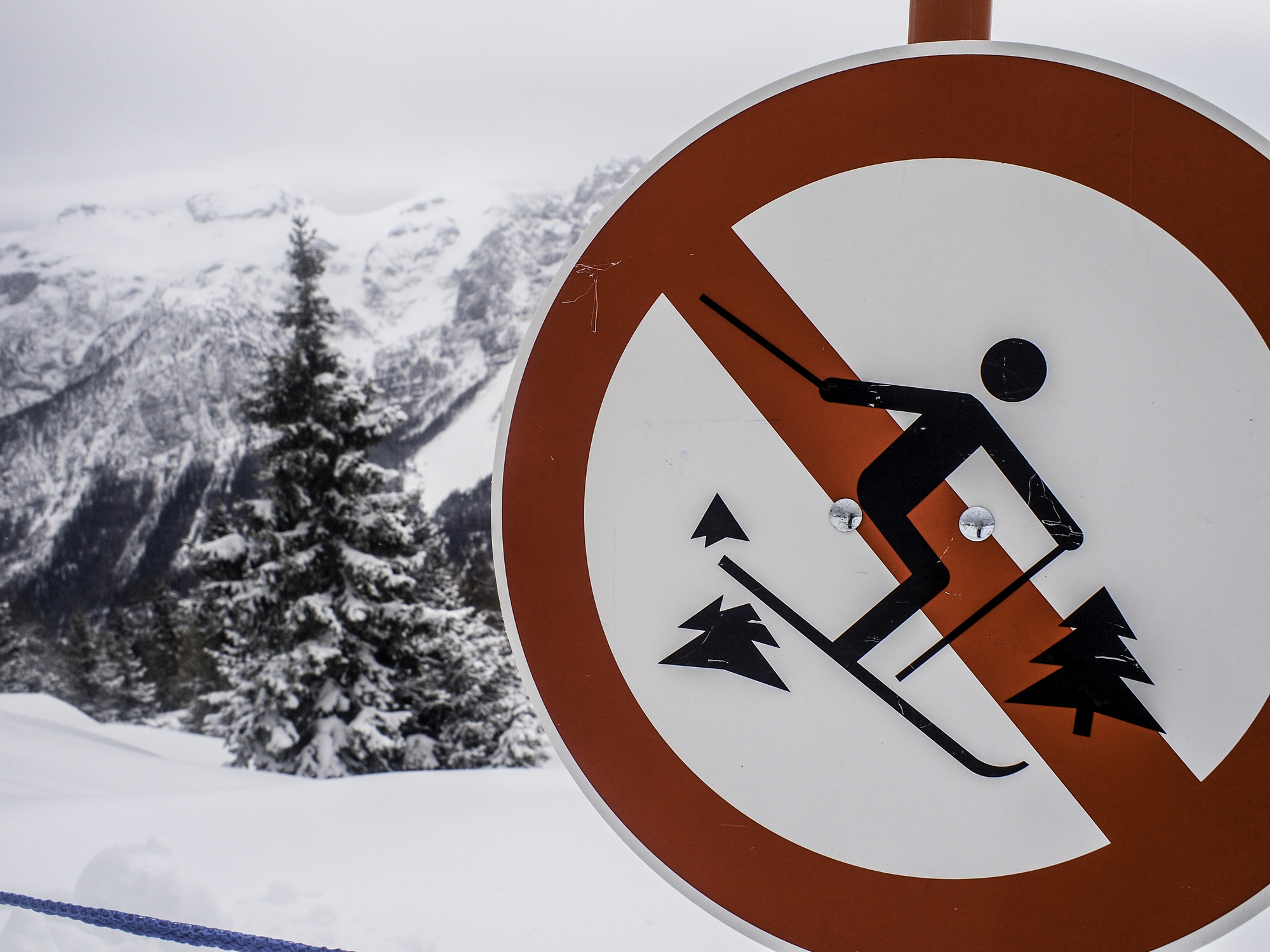 A sign on a snowy mountain showing a skier with a red prohibition symbol, indicating that skiing in the area is not allowed