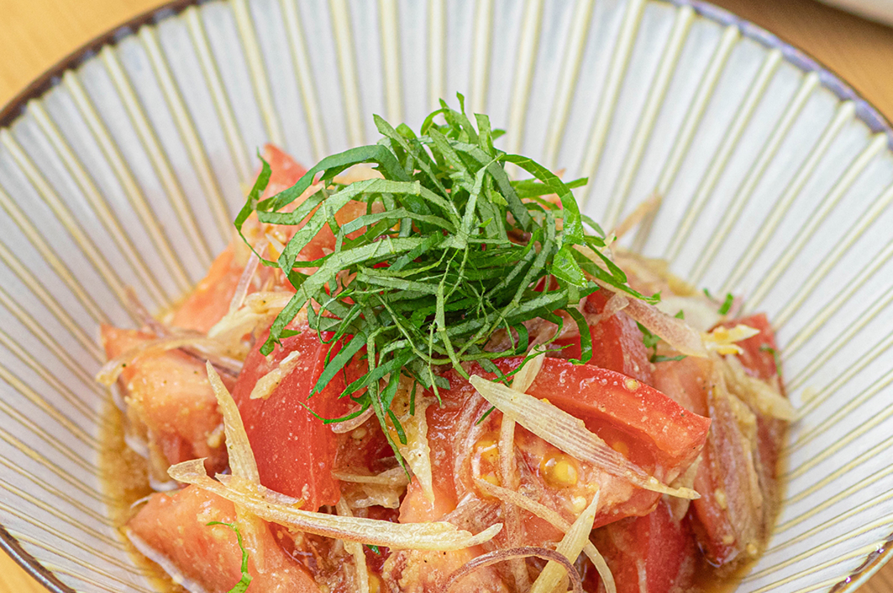 白い皿に盛られたトマトと玉ねぎのサラダ。上には刻んだ大葉が添えられている。