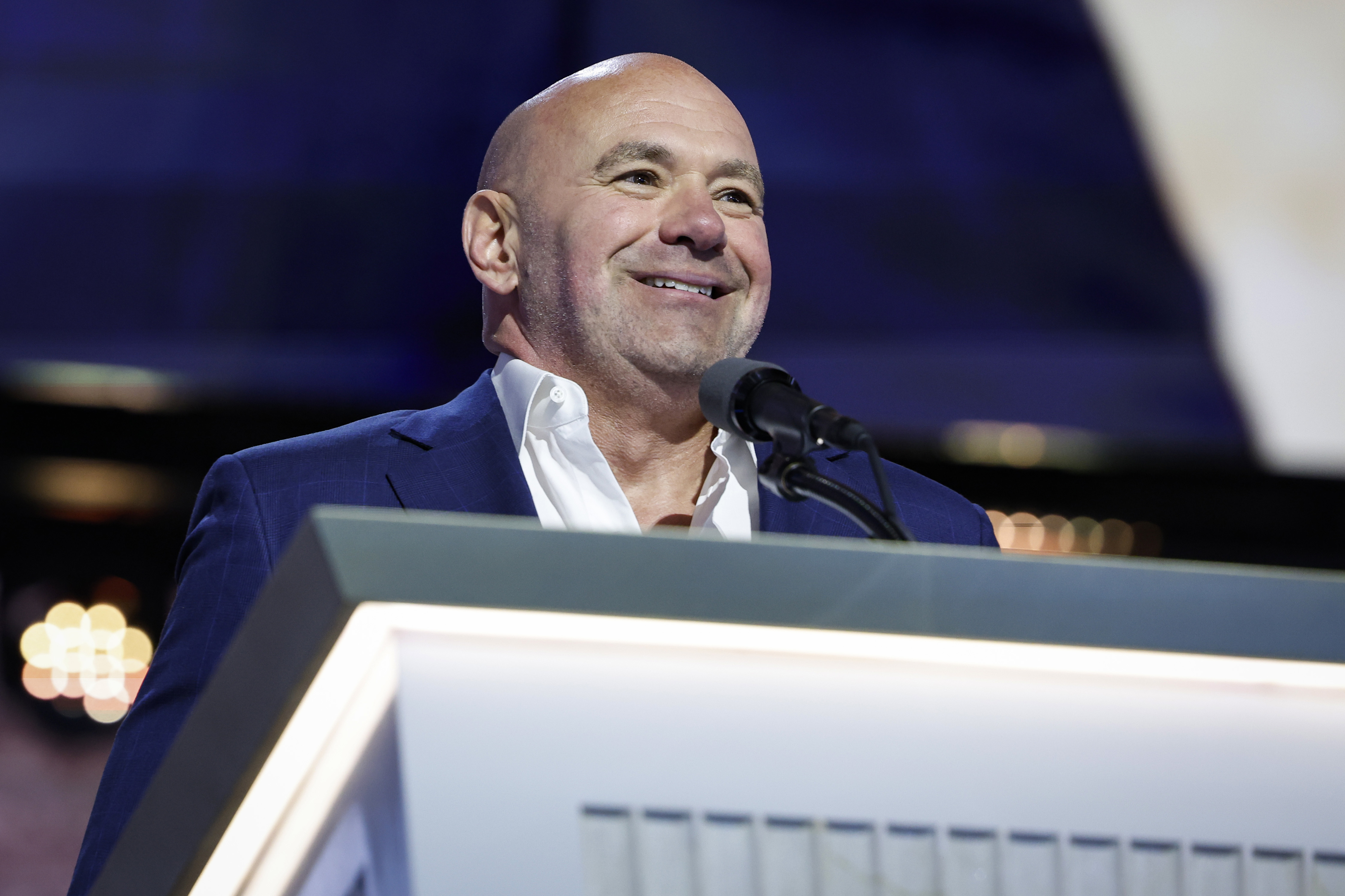 Dana White speaking at a podium, smiling in a formal event setting