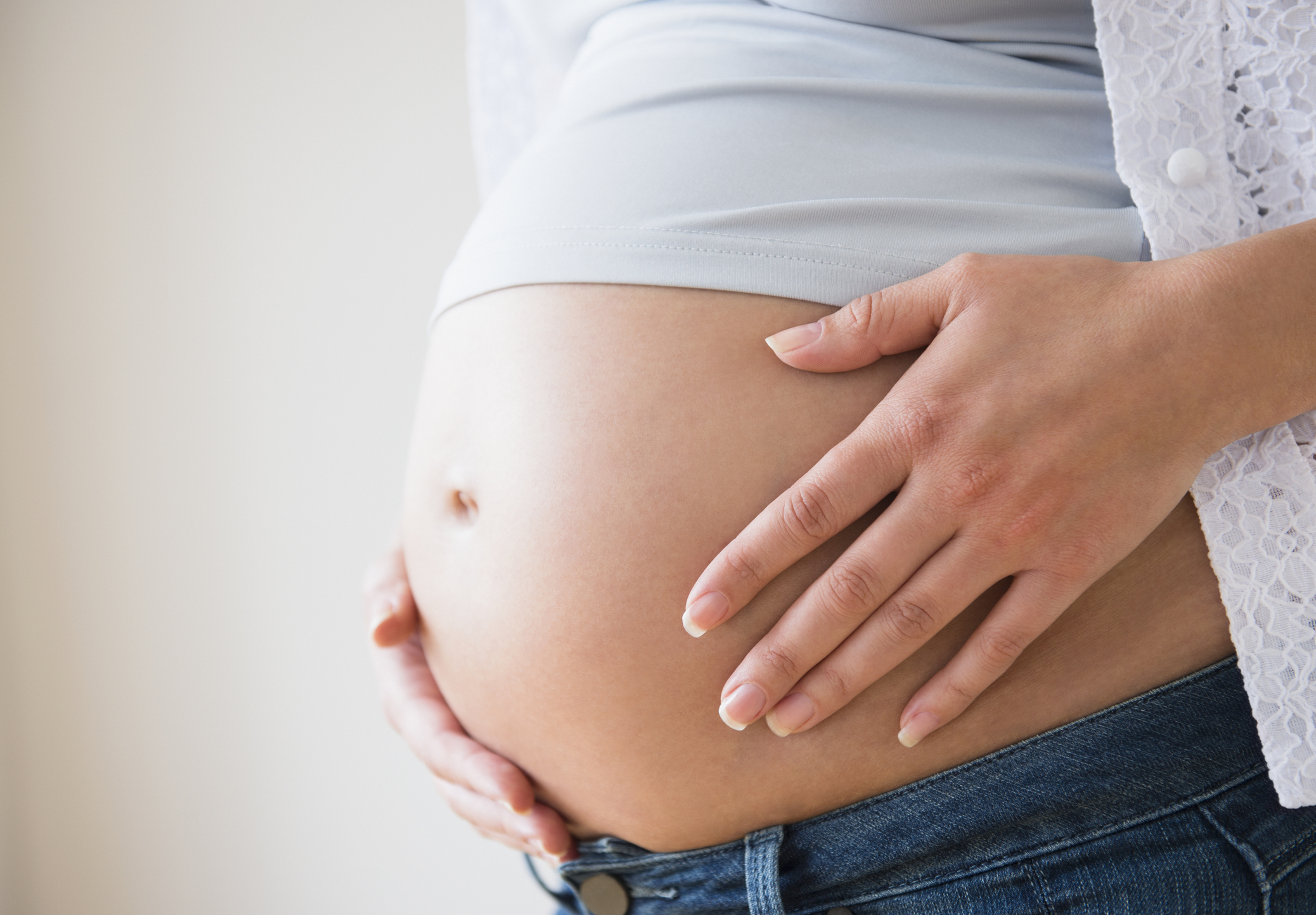 Close-up of a pregnant belly with a person wearing a light shirt and jeans, gently resting hands on the belly