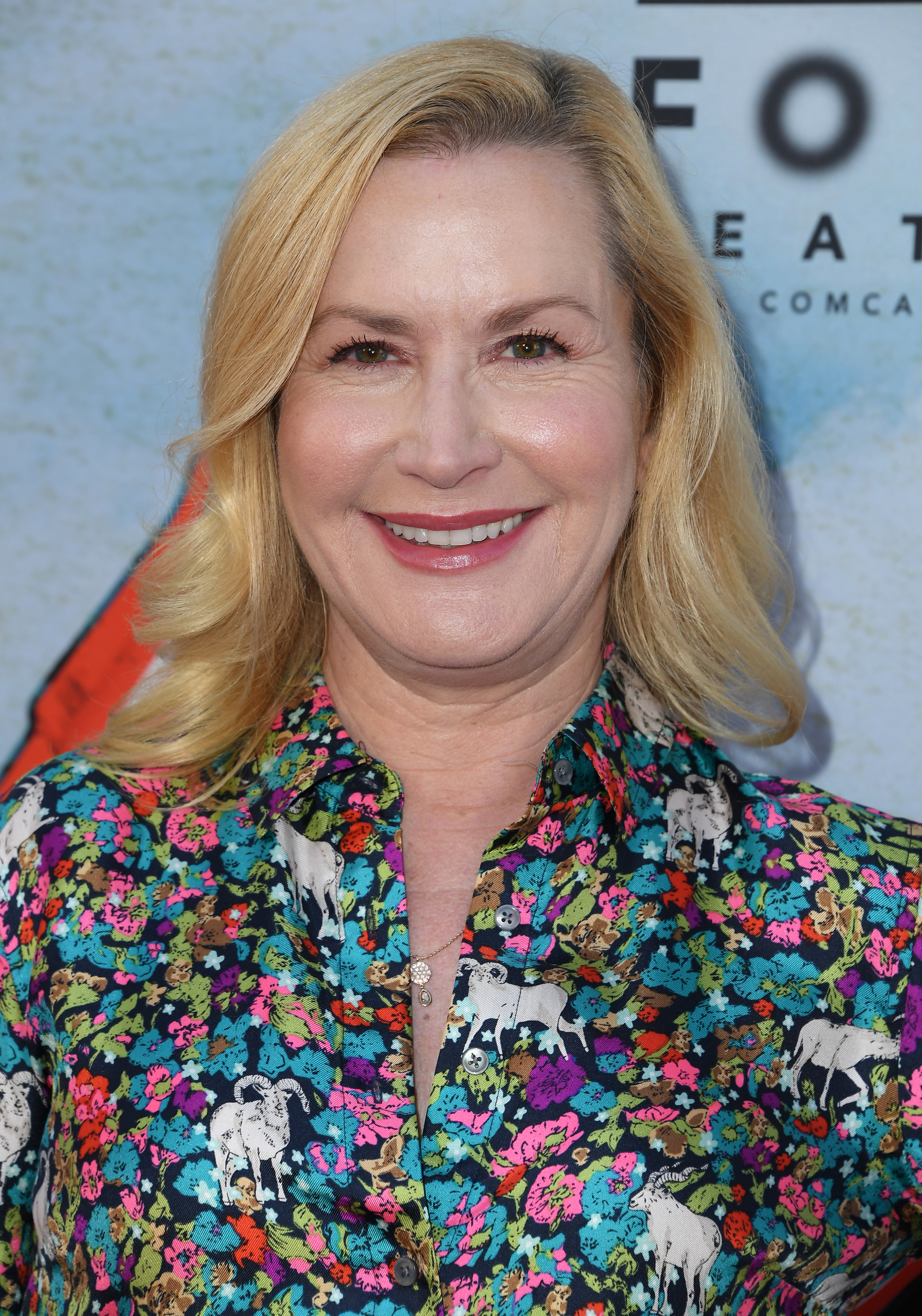 Angela Kinsey smiles at a red carpet event, wearing a floral button-up shirt with a horse pattern