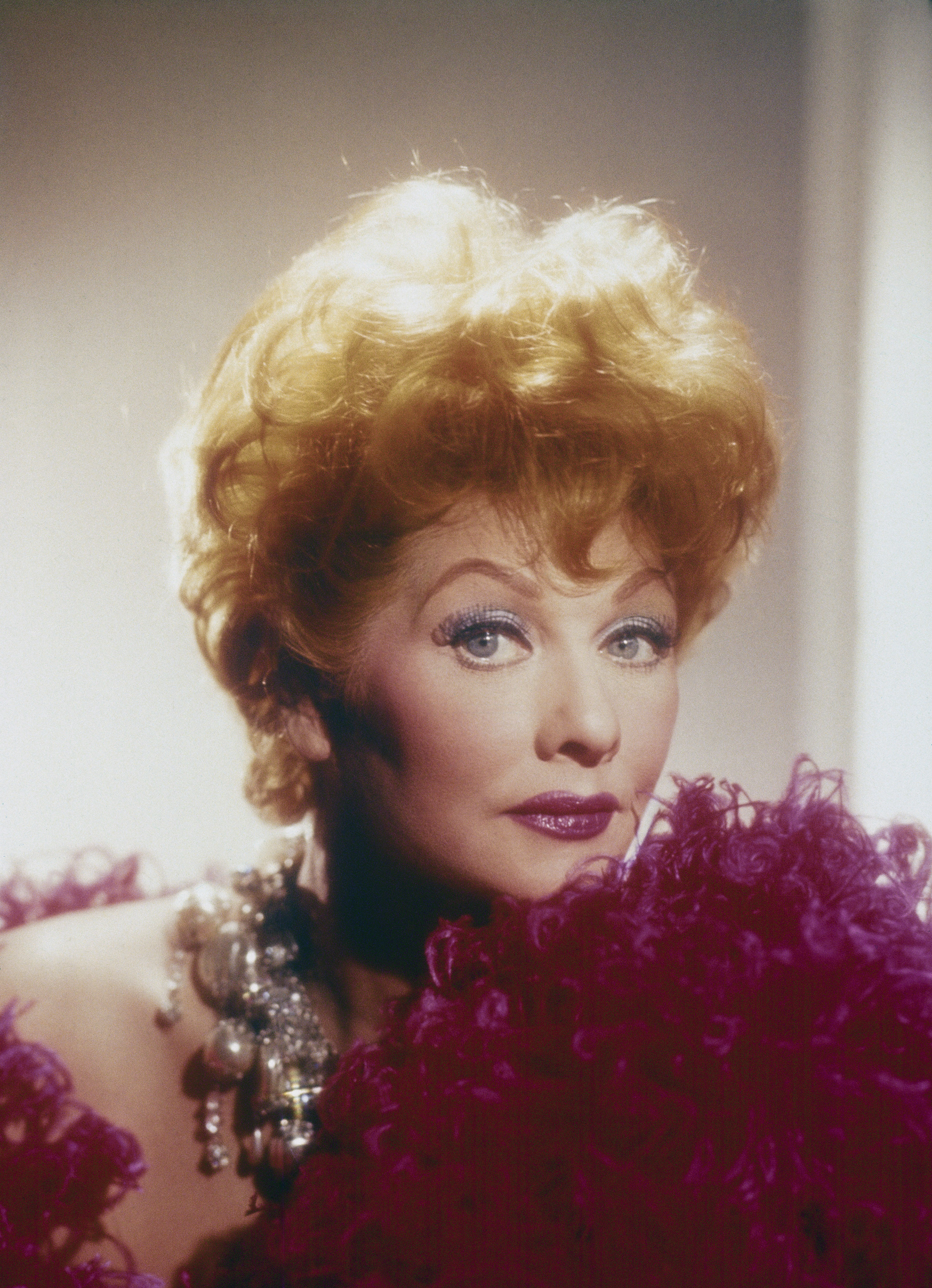 Lucille Ball poses glamorously, wearing a feathered outfit and statement jewelry