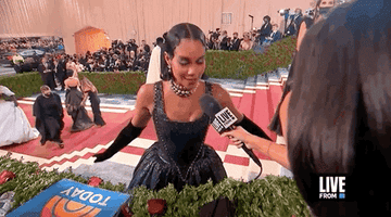 woman at red carpet event, being interviewed. She wears a strapless gown with matching gloves and a sparkling choker necklace