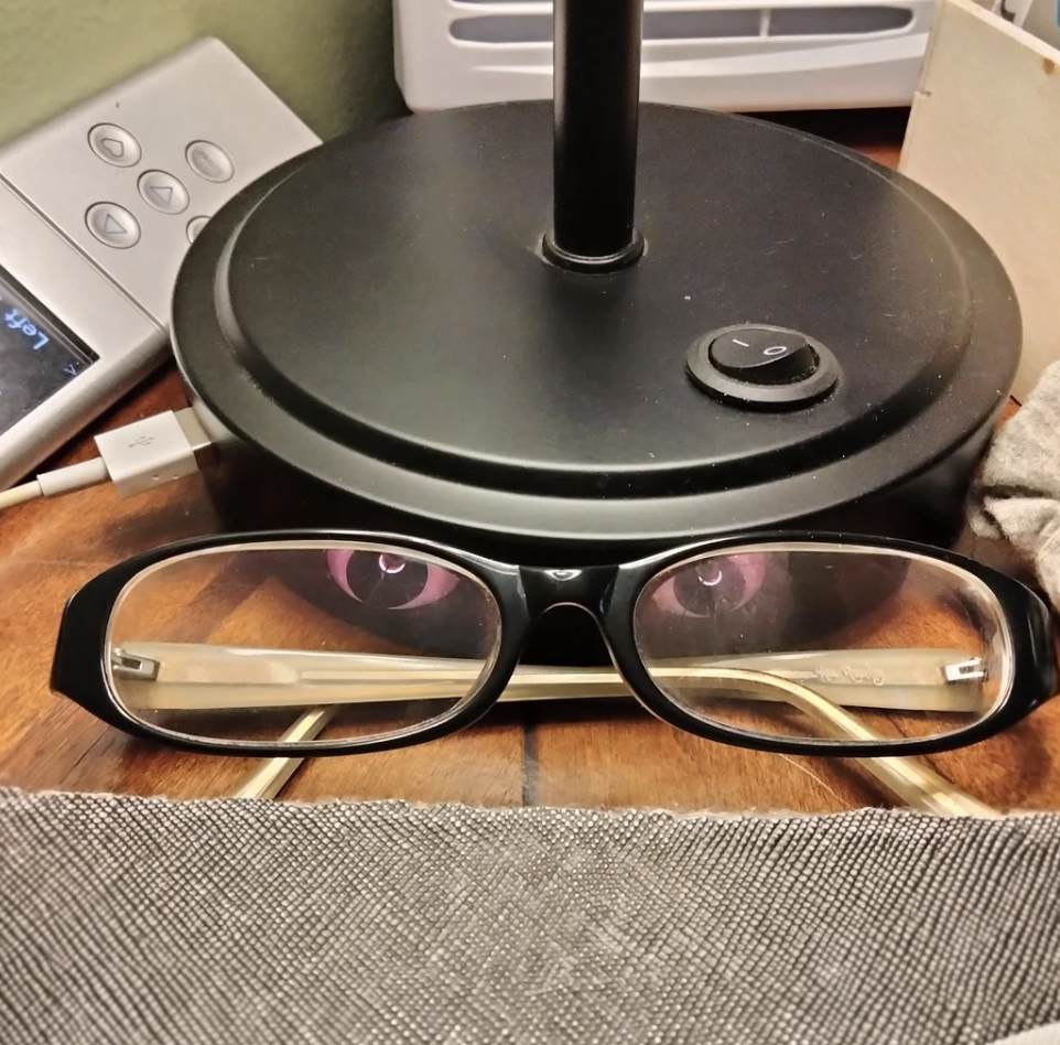 A pair of glasses is placed in front of a small black lamp, creating an illusion of a face with eyes reflected on the lamp's base
