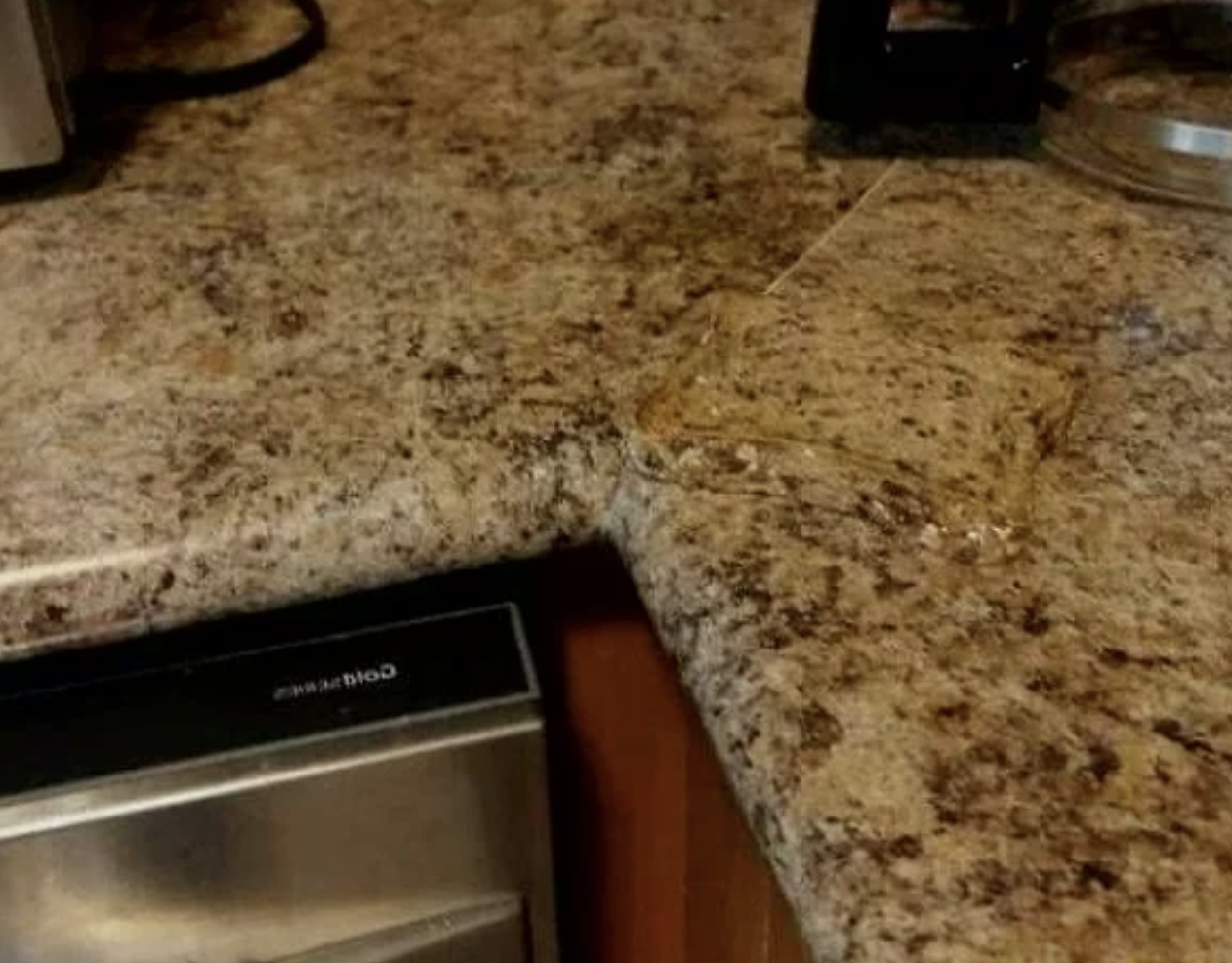 A glass dish on a granite kitchen countertop next to a stainless steel dishwasher