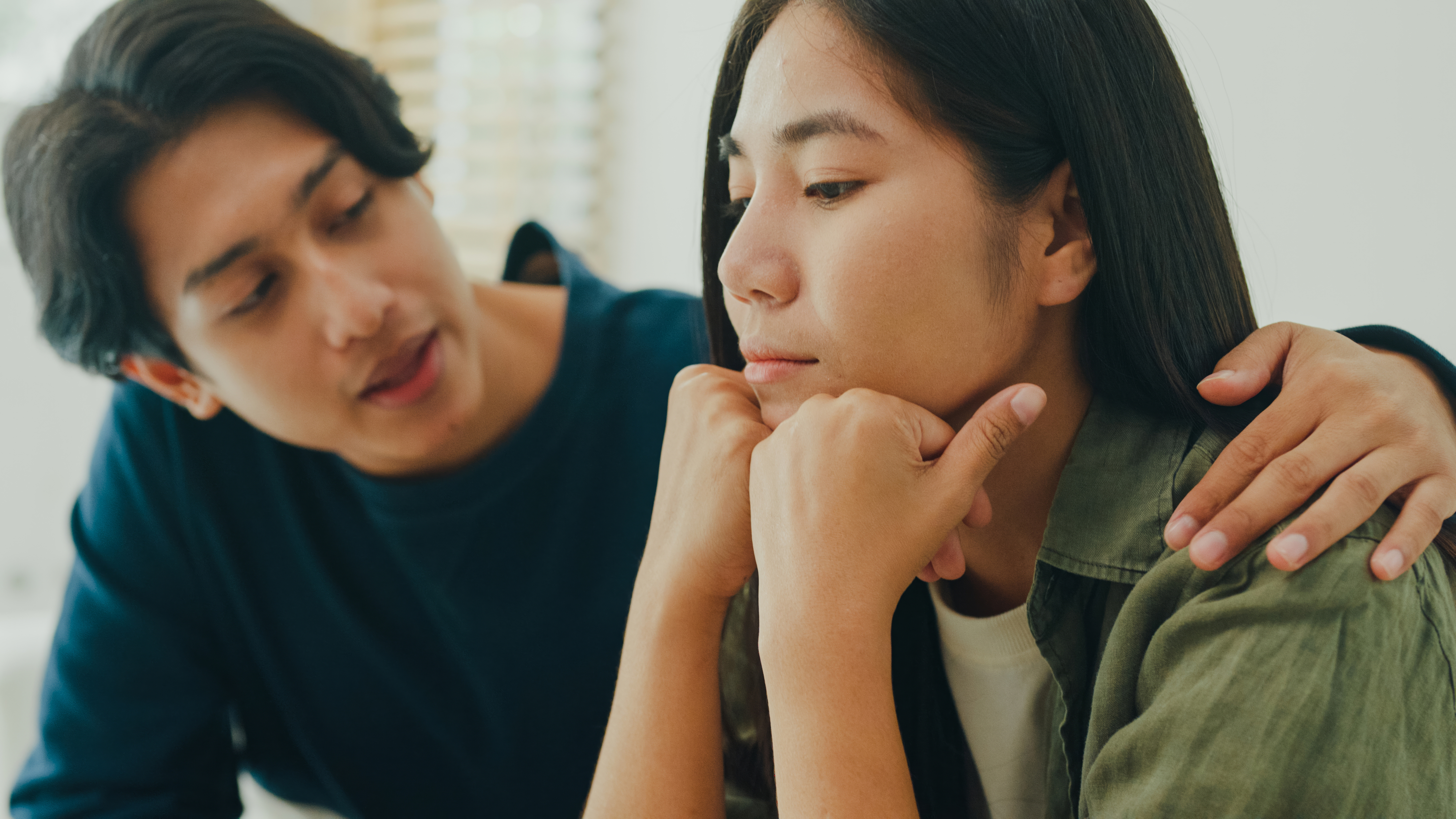 Two people, a man and a woman, are sitting together. The man is comforting the woman with a hand on her shoulder