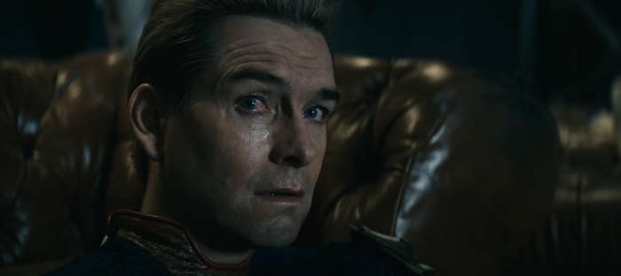 The image shows a close-up of Homelander from &quot;The Boys,&quot; with a serious expression while seated on a leather couch