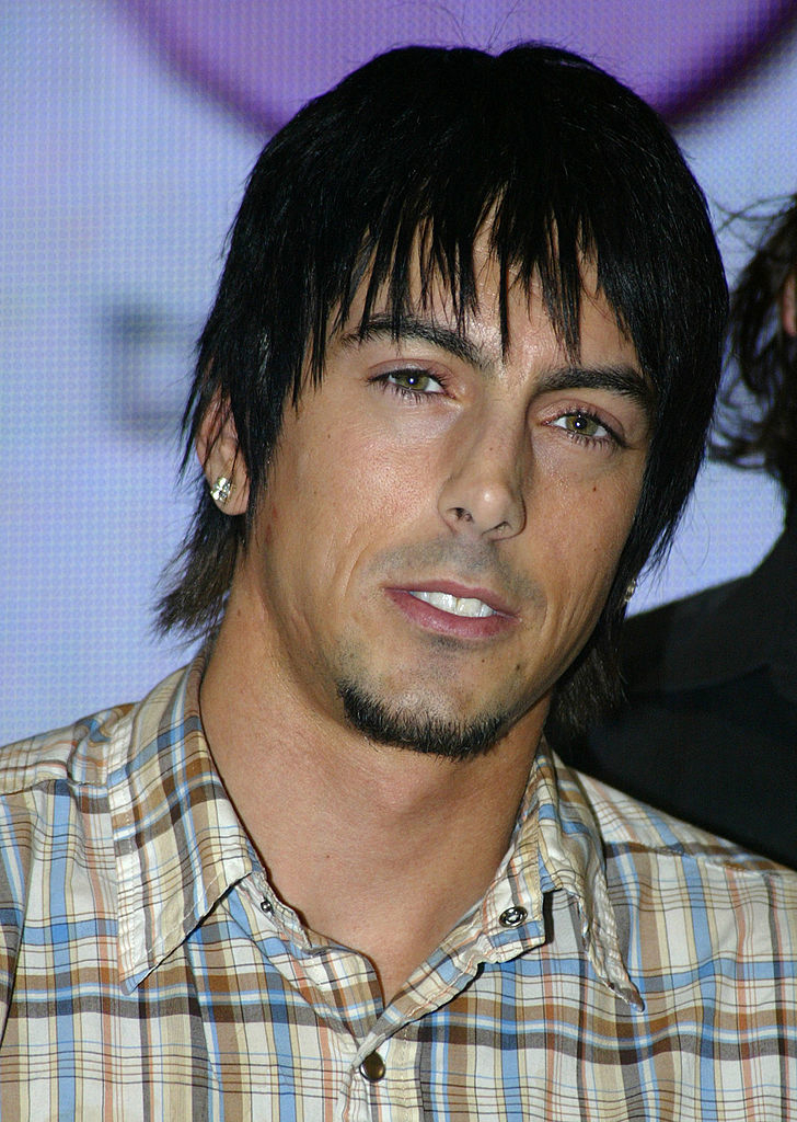 A man with short, dark hair and a goatee smiles while wearing a plaid button-up shirt