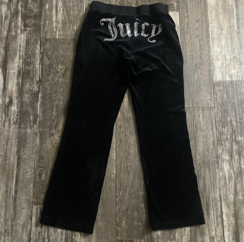 Black Juicy Couture velour pants with &quot;Juicy&quot; written in rhinestones on the back. Pants are laid out flat on a wooden floor