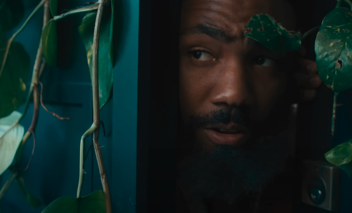 Donald Glover peeking through a doorway surrounded by green leaves and vines