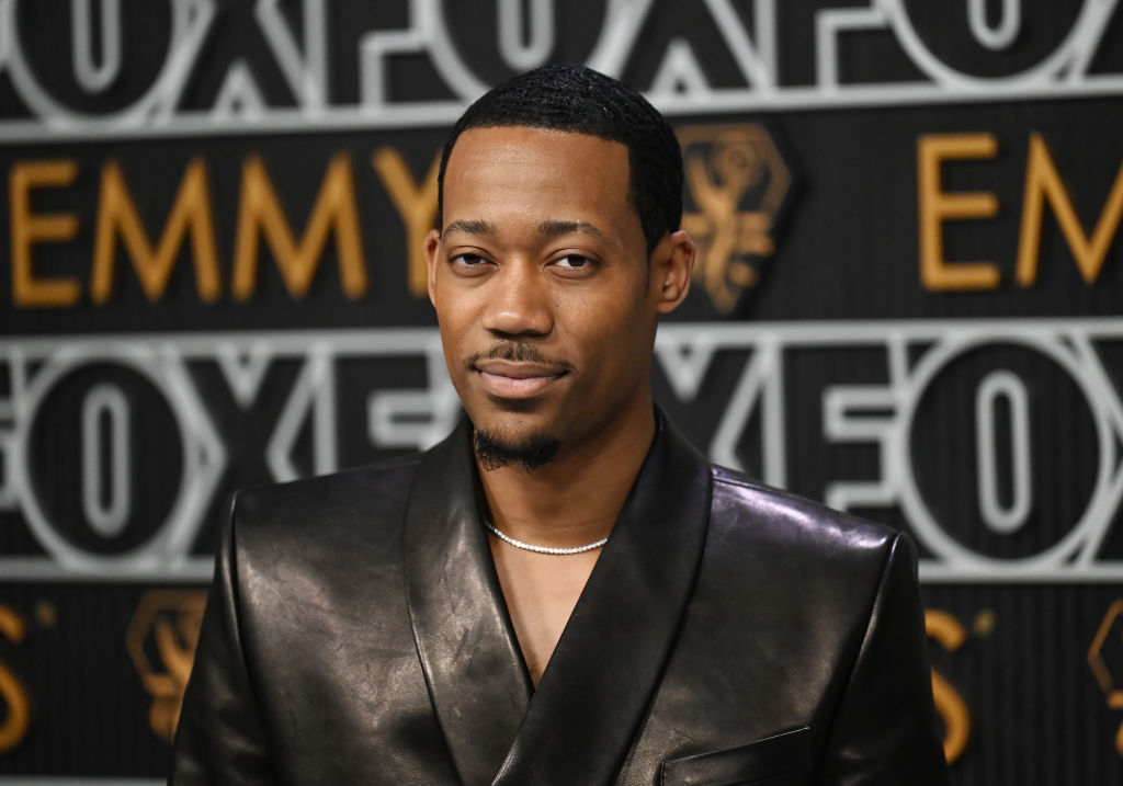 A person in a black leather suit stands in front of a background with "FOX" and "EMMY" text