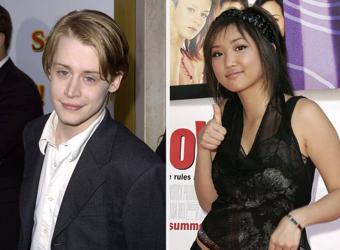 Macaulay Culkin in a suit next to Brenda Song in a sheer black top giving a thumbs-up at an event