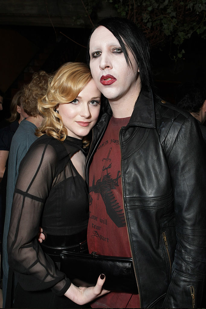 Evan Rachel Wood in a sheer-sleeved dress with black accessories, and Marilyn Manson in a leather jacket and printed t-shirt, posing together at an event