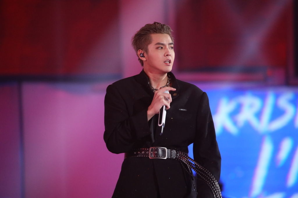 Kris Wu performing on stage, wearing a dark belted outfit and holding a microphone
