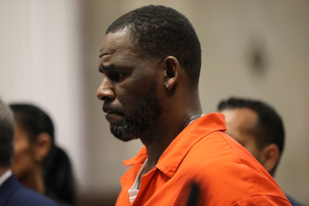 R. Kelly, wearing an orange jumpsuit, stands with a serious expression during a courtroom hearing