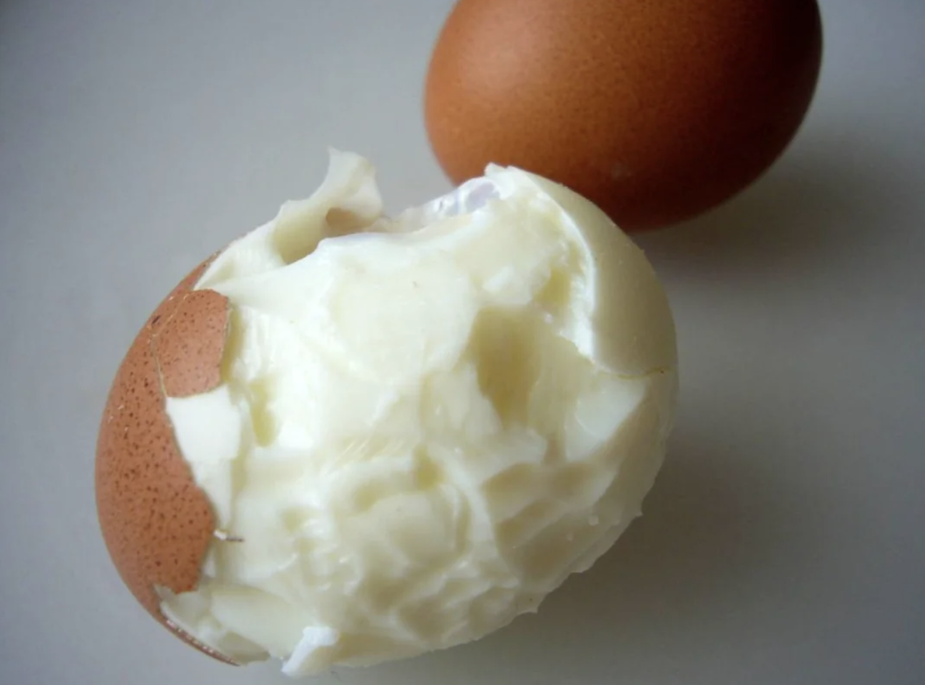 Partially peeled hard-boiled egg with significant chunks bitten off, revealing the white interior. Another whole egg is visible in the background