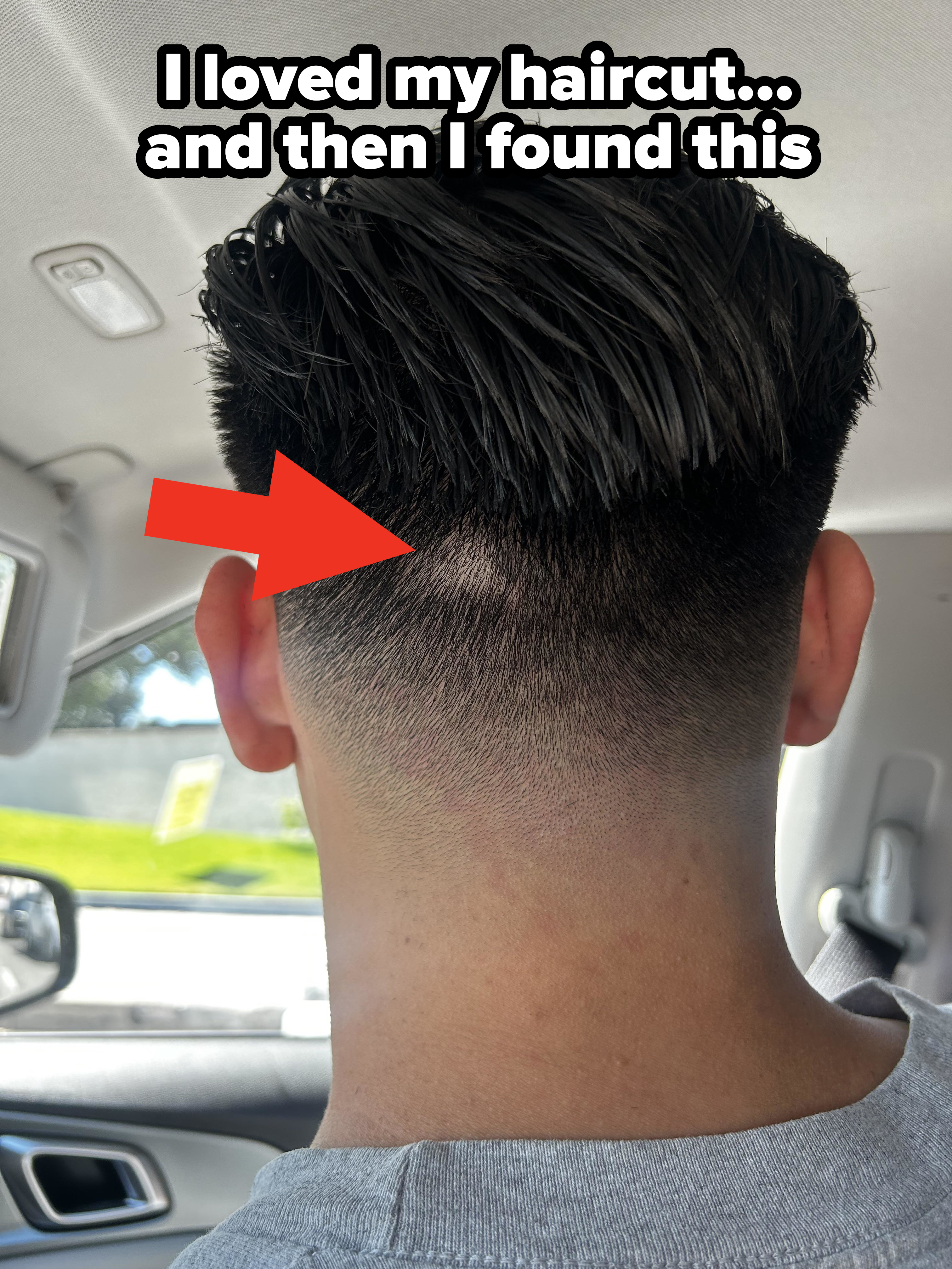 The image shows the back of a person's head with a clean, well-groomed haircut featuring a tapered fade. The person is sitting inside a car