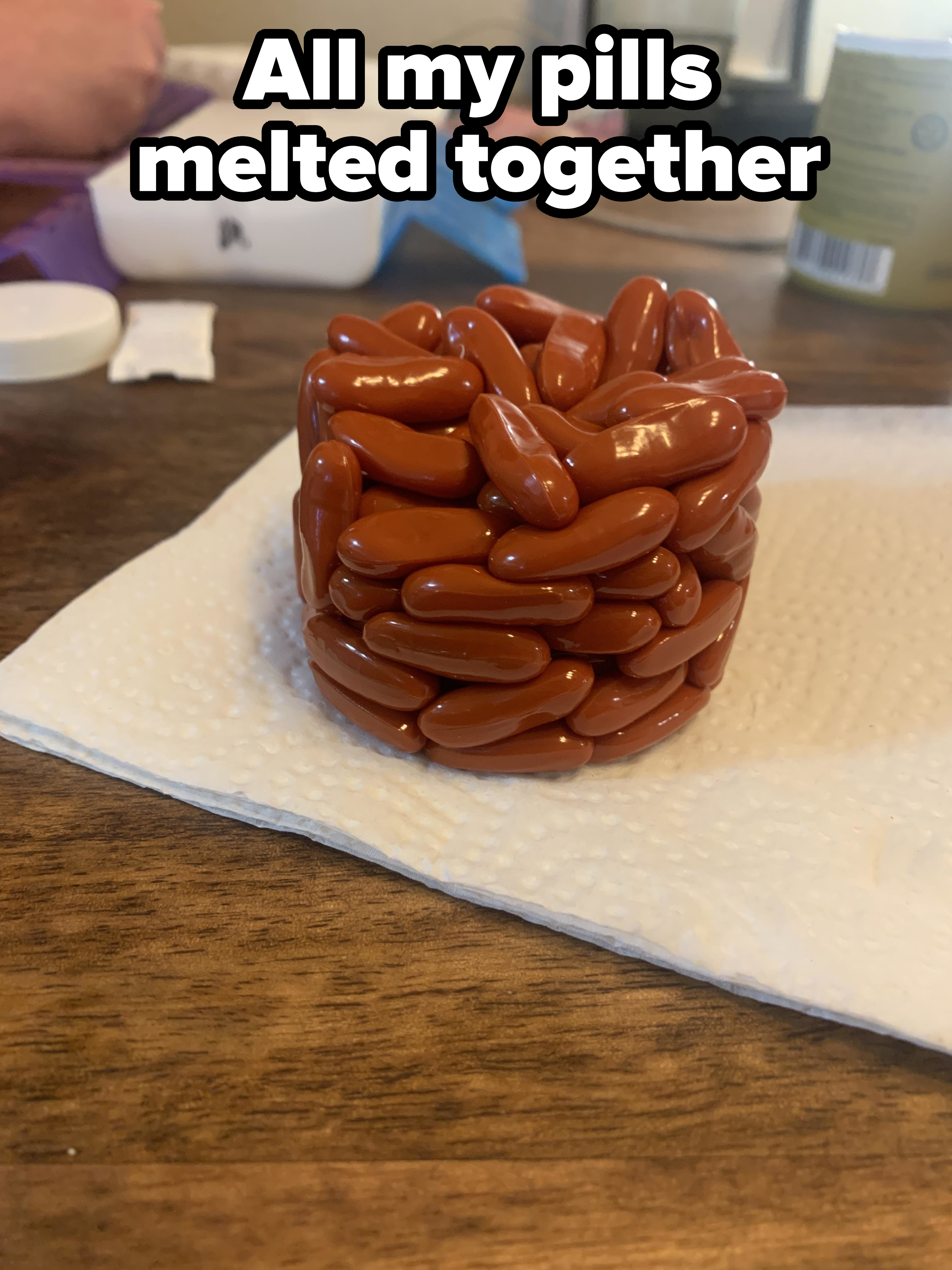A cylindrical stack of red pills on a paper towel on a wooden table. Various containers and objects are blurred in the background