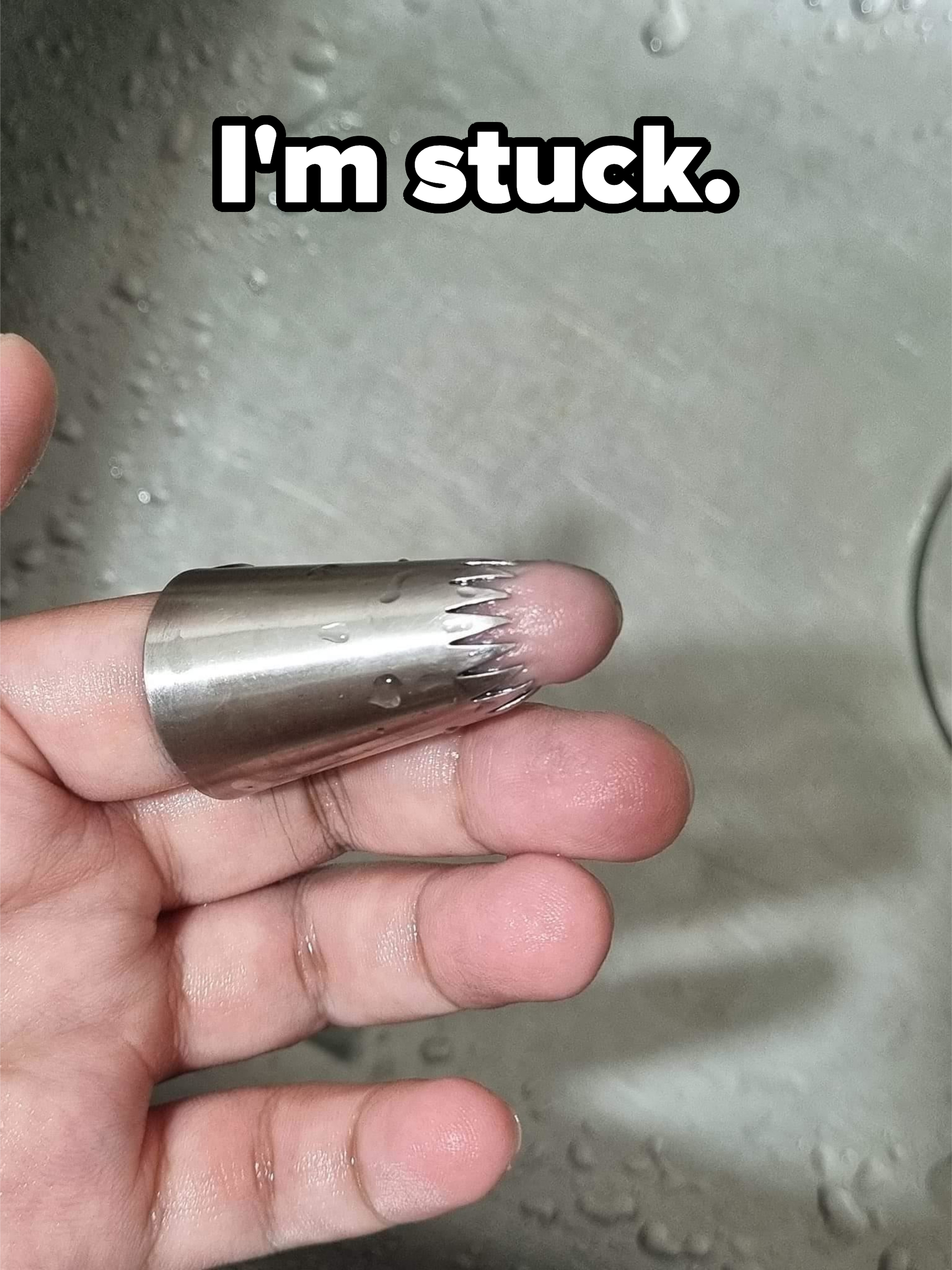 A person is holding a piping tip on their fingertip, making it look like the finger has spiky metal edges