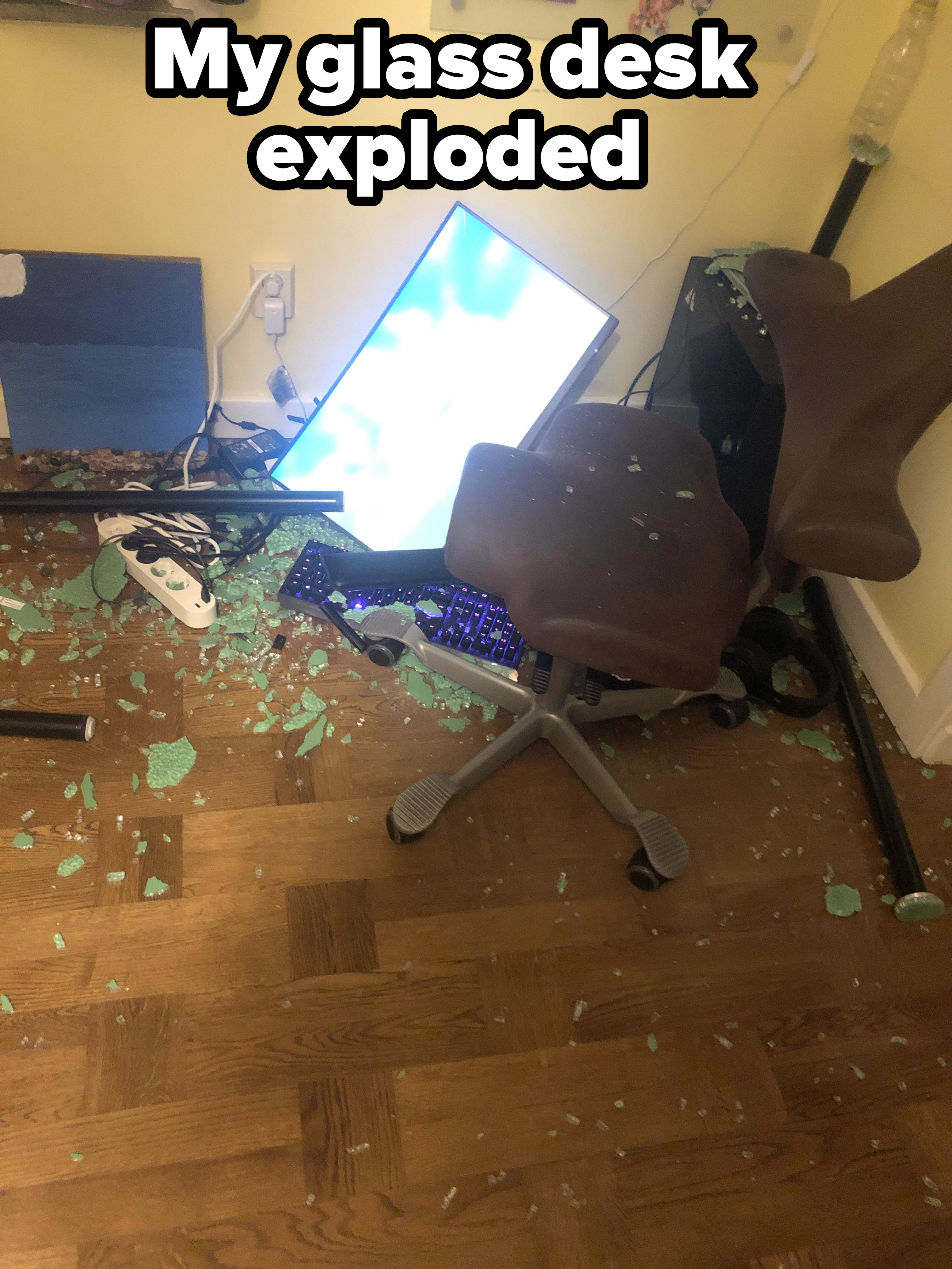 A small office area with a broken computer monitor on the floor, shattered glass, a fallen chair, and scattered debris
