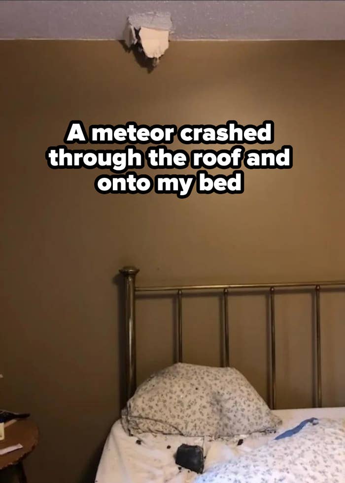 A bed with floral-patterned pillows and a brass headboard sits against a beige wall with a hole in the ceiling above it. Debris is on the bed