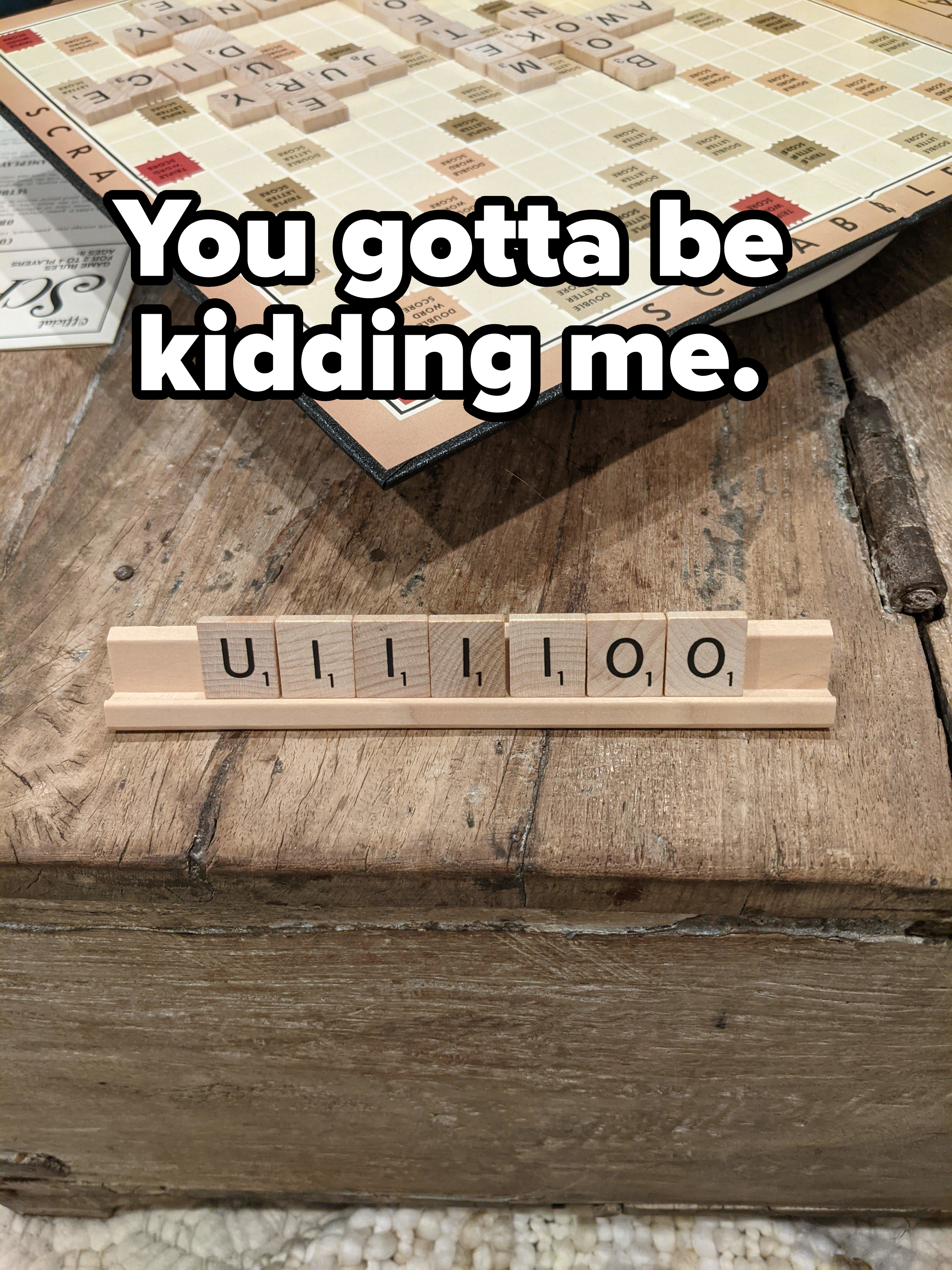 Scrabble game in progress, player's tiles form "ULLLIOO" on a wooden tile rack. Scrabble board visible in the background