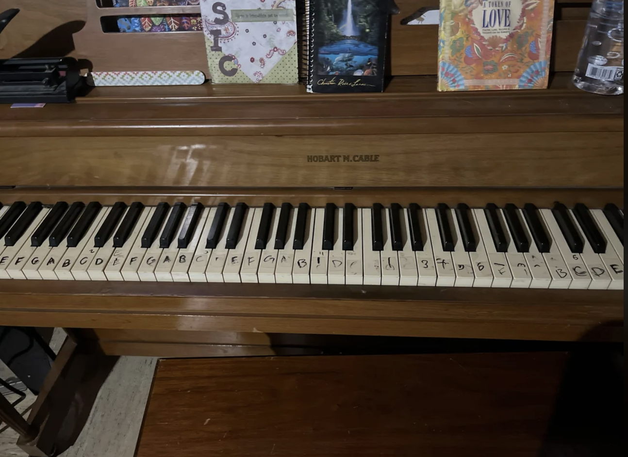 A piano keyboard with note labels written on the keys, featuring books and other items on top