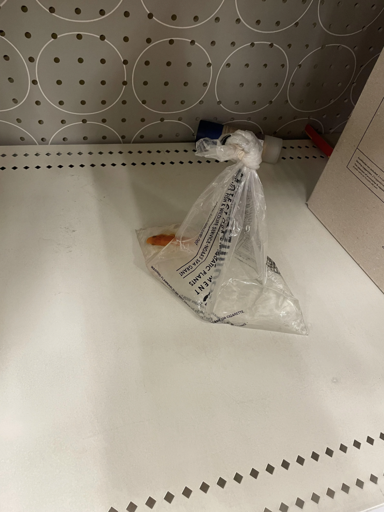 A clear plastic bag filled with water and an orange object inside, placed on a perforated white metal surface