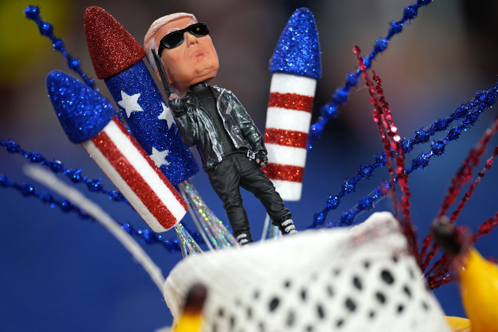 A bobblehead of President Joe Biden in a leather jacket and sunglasses is surrounded by rocket decorations, resembling a patriotic theme