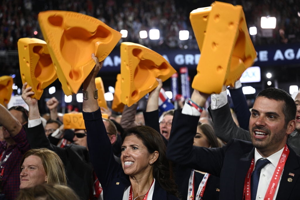 Crowd at an event holds up large, foam cheese hats. Unidentified individuals celebrate enthusiastically. The background includes the text &quot;GREAT AGAIN.&quot;
