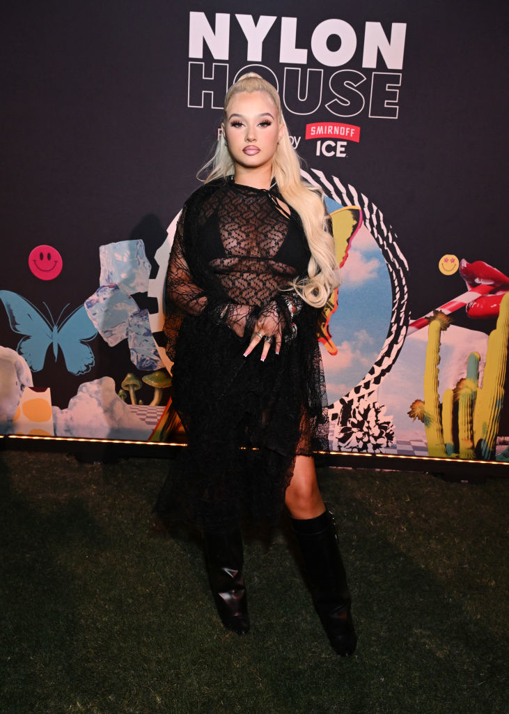 Alabama Barker poses on the red carpet at the Nylon House event by Smirnoff Ice, wearing a lace dress with long sleeves and knee-high boots