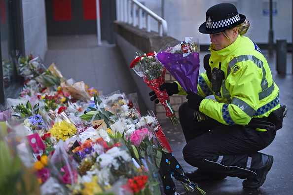 Police officer examines flowers and tributes laid out on the ground