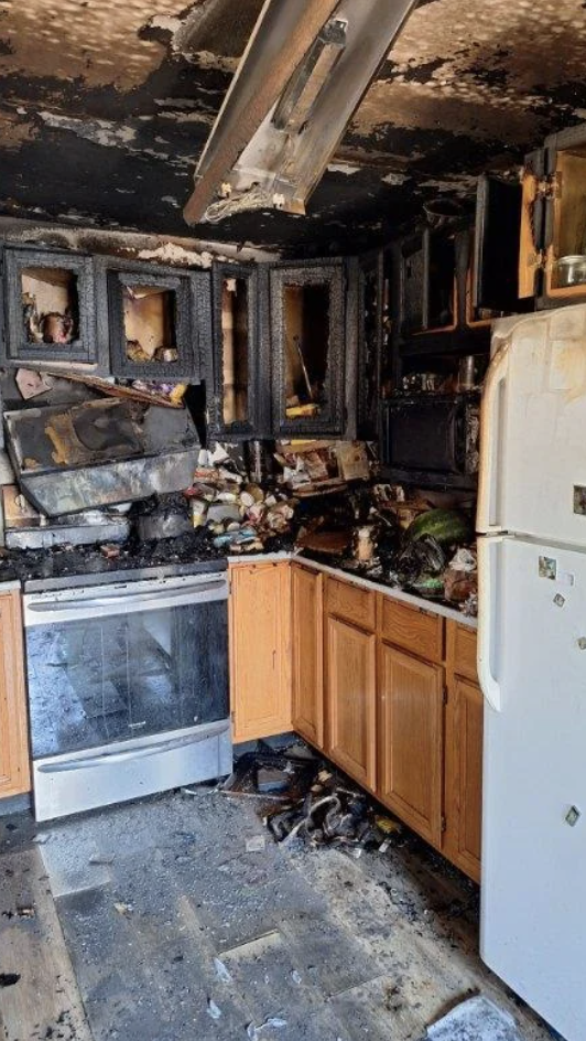 Burned kitchen with charred cabinets, melted appliances, and significant fire damage throughout. No people present in the image