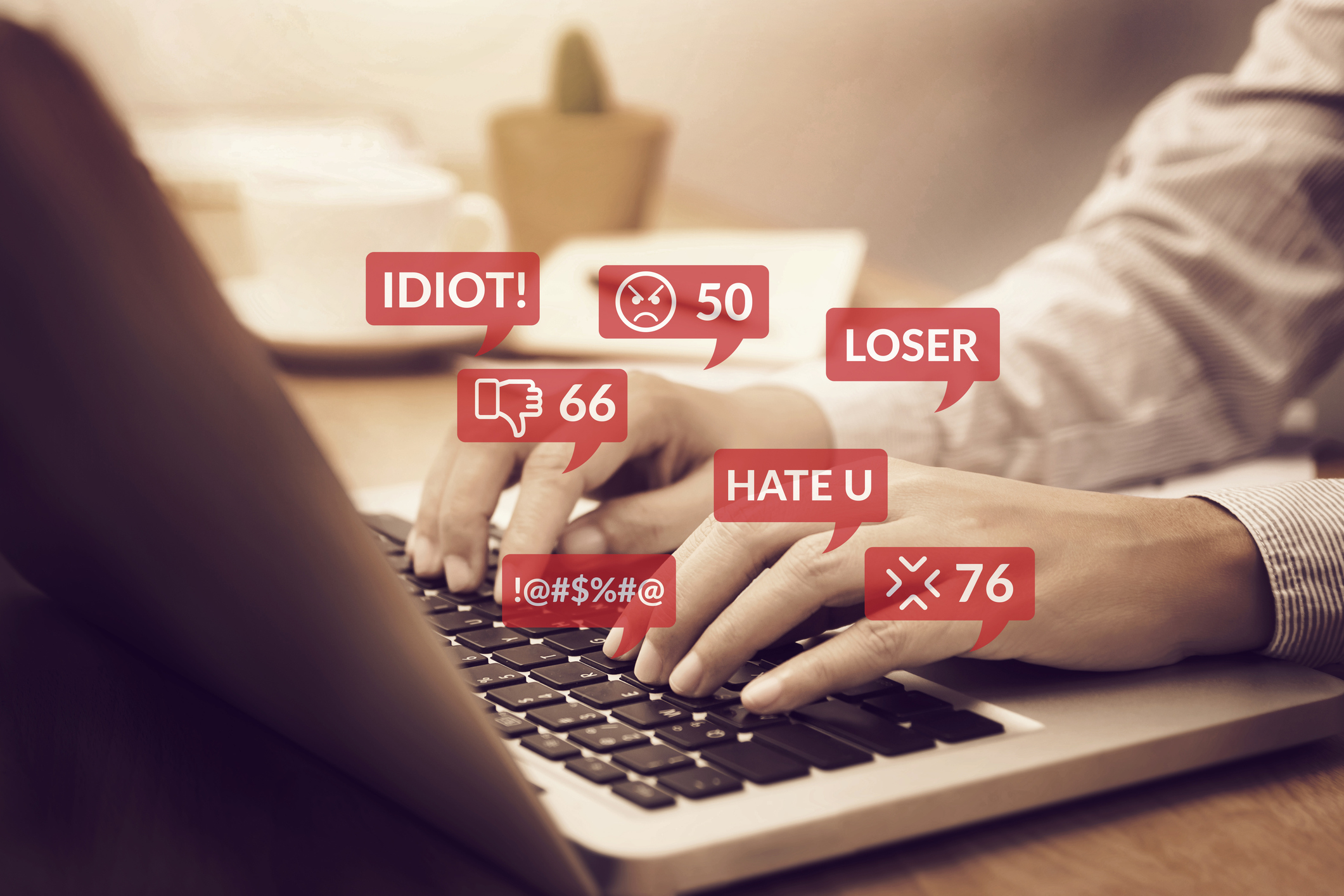 Hands typing on a laptop while numerous negative comments like "IDIOT!", "LOSER", "HATE U", and others appear on screen, indicating online harassment