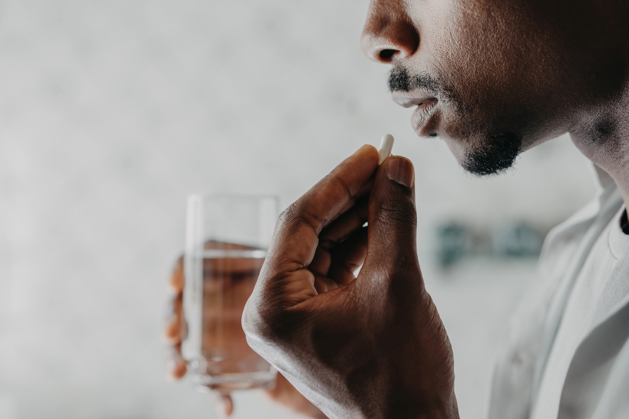 A person holds a pill near their lips with one hand and a glass of water in the other hand, appearing to be about to take the pill