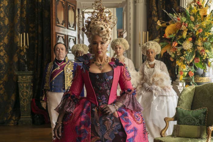 Golda Rosheuvel portrays Queen Charlotte in an ornate period costume with elaborate hair, accompanied by four characters dressed in luxurious attire in a regal setting